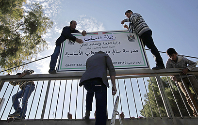 מחליפים שלט לבית ספר עם הכותרת "מדינת פלסטין" (צילום: AFP)
